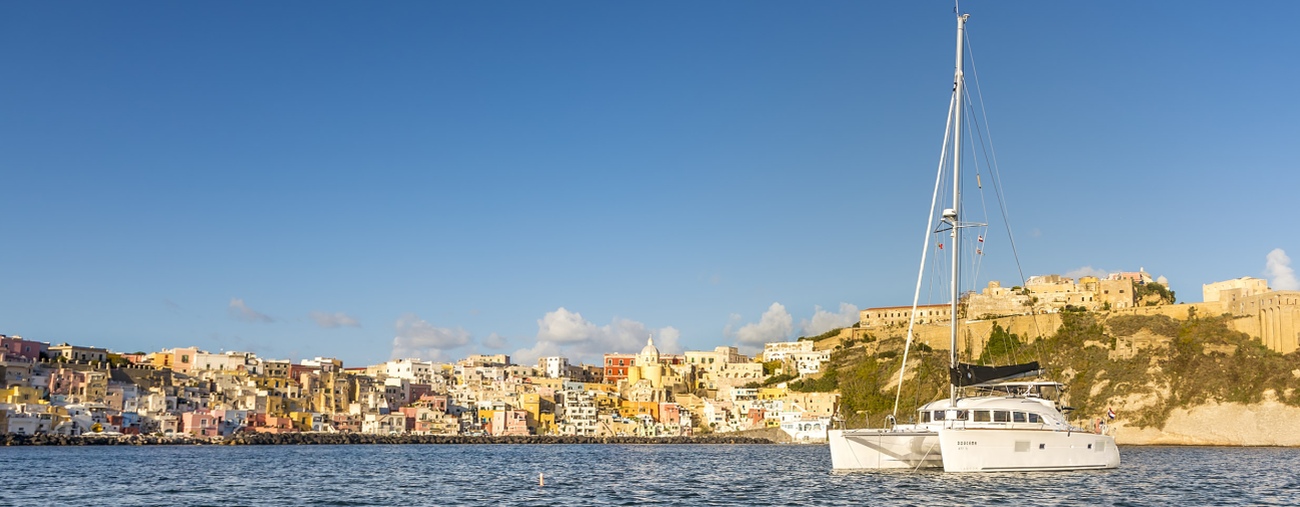 Ankern vor typisch süditalienischer Hafenkulisse - Der Katamaran Doucema liegt vor Procida im Golf von Neapel. Foto: Gerald Winkler ein Katamaran ankert vor der sonnenbeschienenen Hafenkulisse in Süditalien